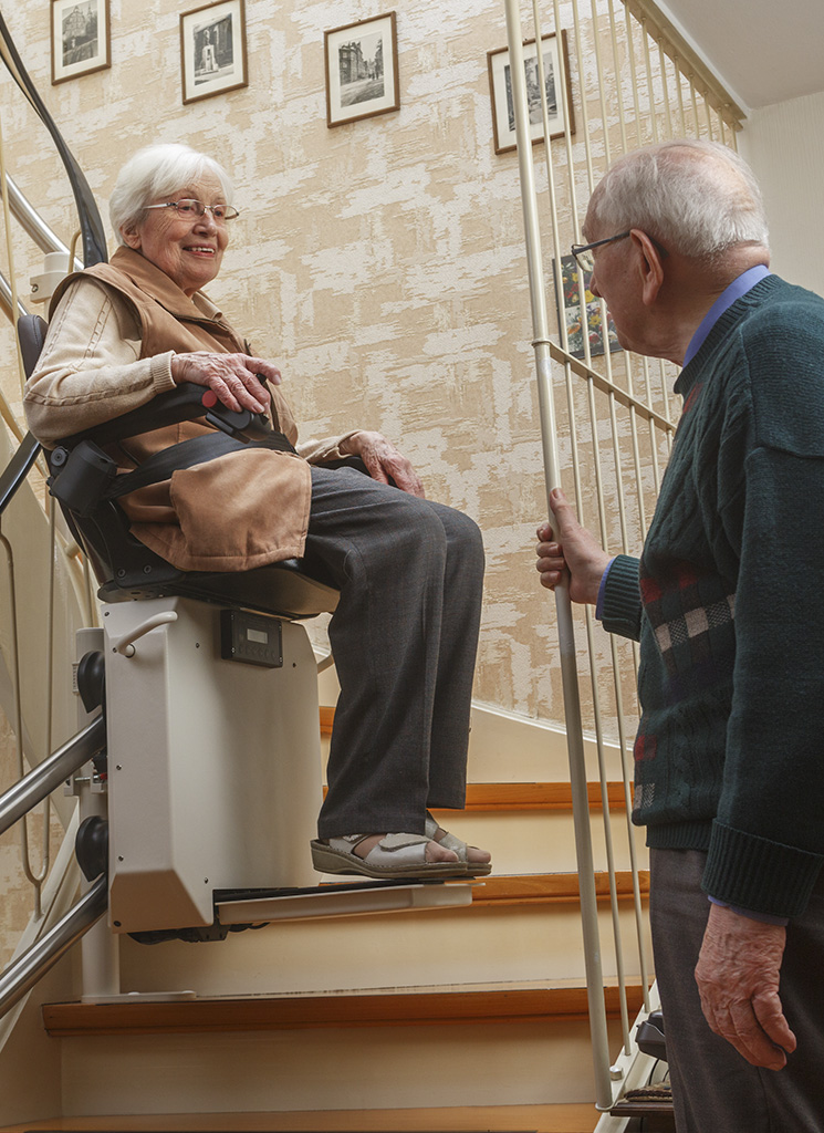 Frau Sitz in einem eingebauten Treppenlift, Mann schaut zu